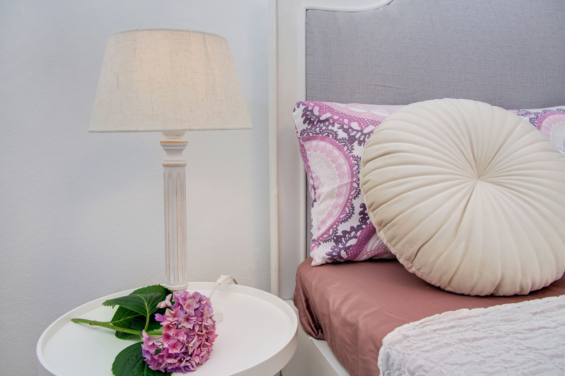 detailbild bett mit rundem kopfkissen lila horthensie auf nachttisch in apartment