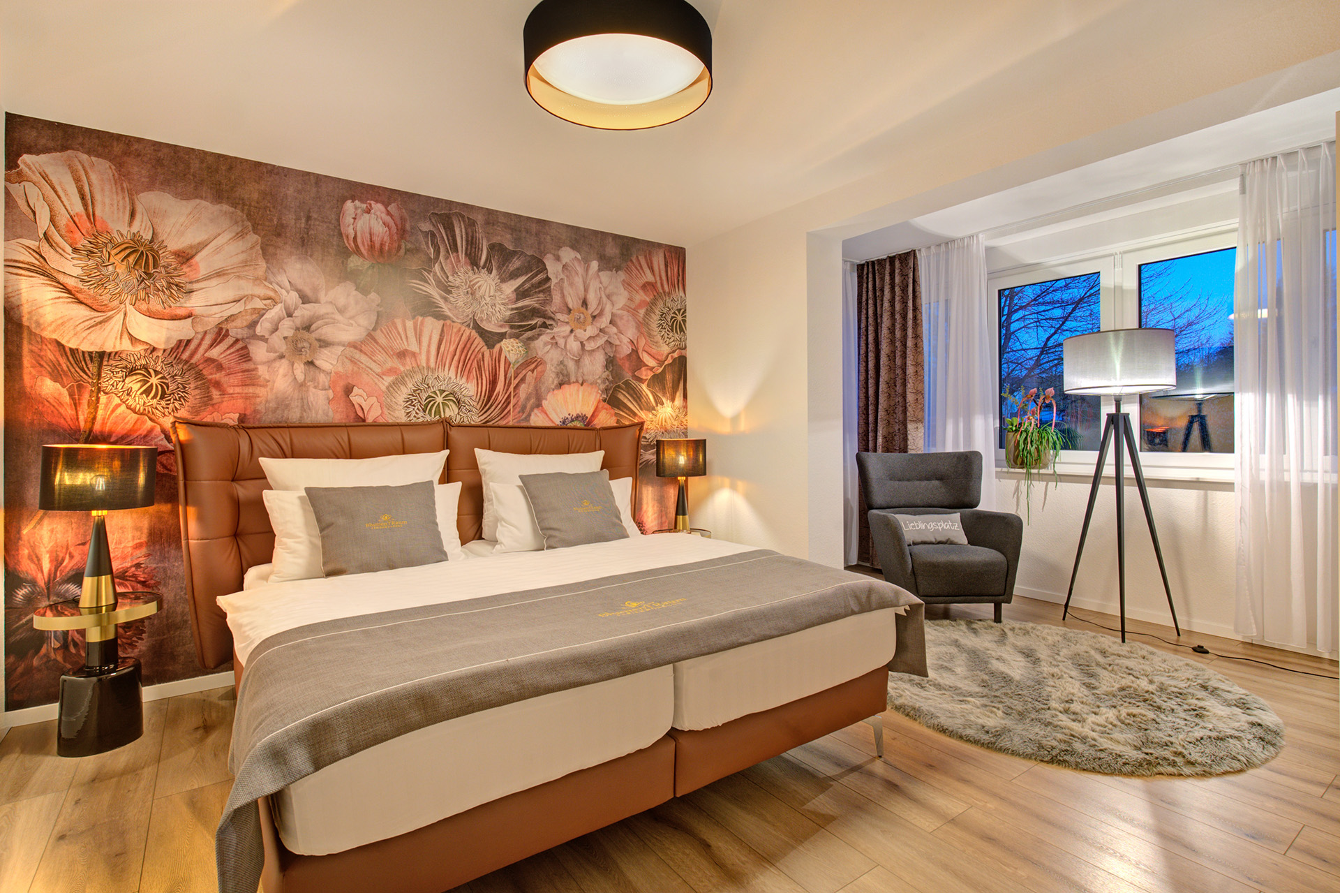 doppelzimmer der ferienwohnung mit grossem blumenmotiv über kopfteil sowie beleuchtete leseecke am abend - vom airbnb fotograf