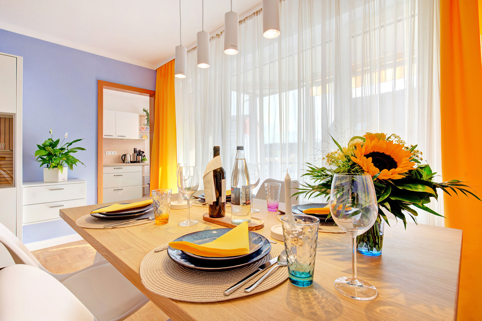 gedeckter esstisch mit sonnenblumenstrauss und blick auf balkonfenster und küche