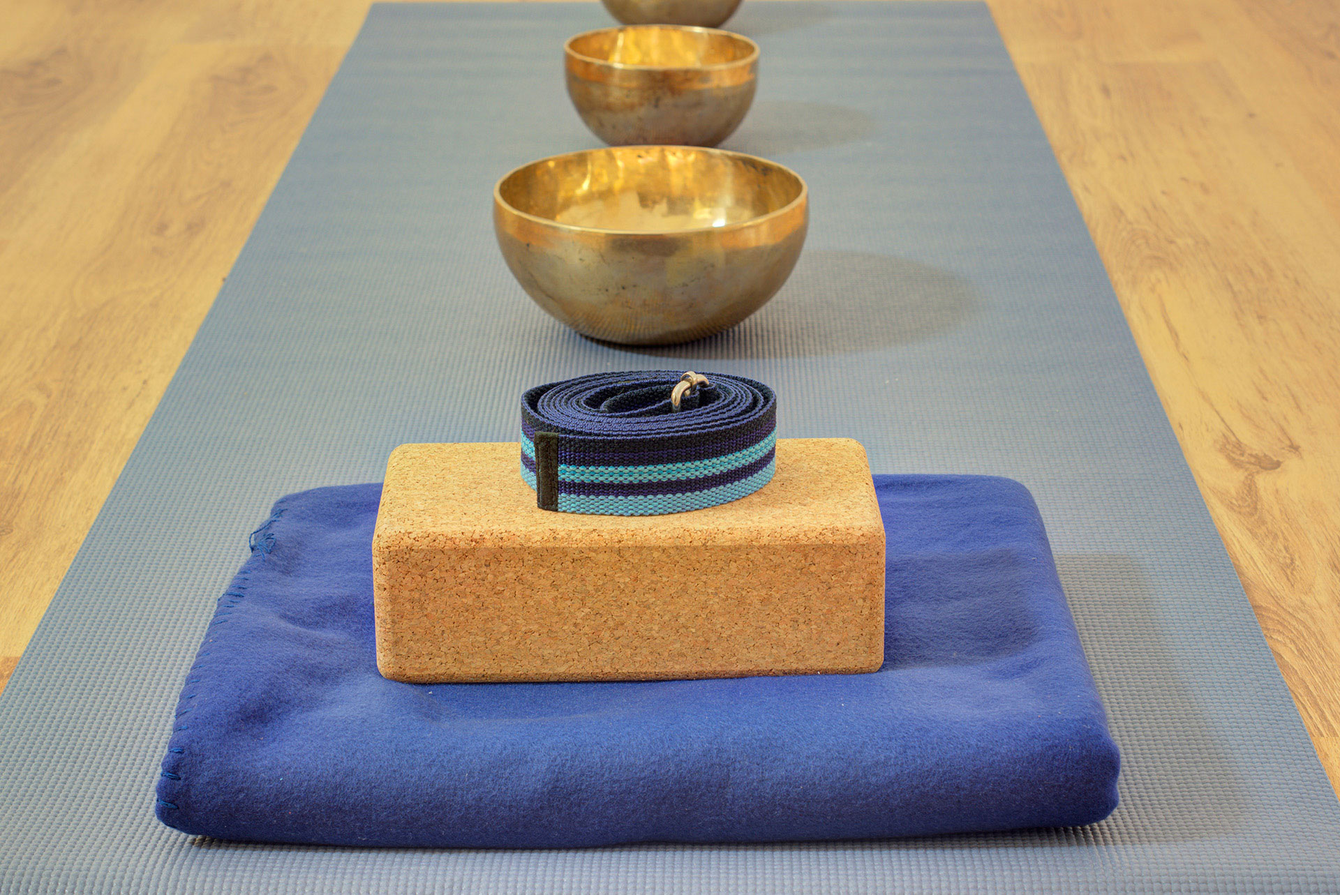 fotografie yoga studio  yogamatte mit blauer decke korkblöcke riemen und klangschalen hintereinander
