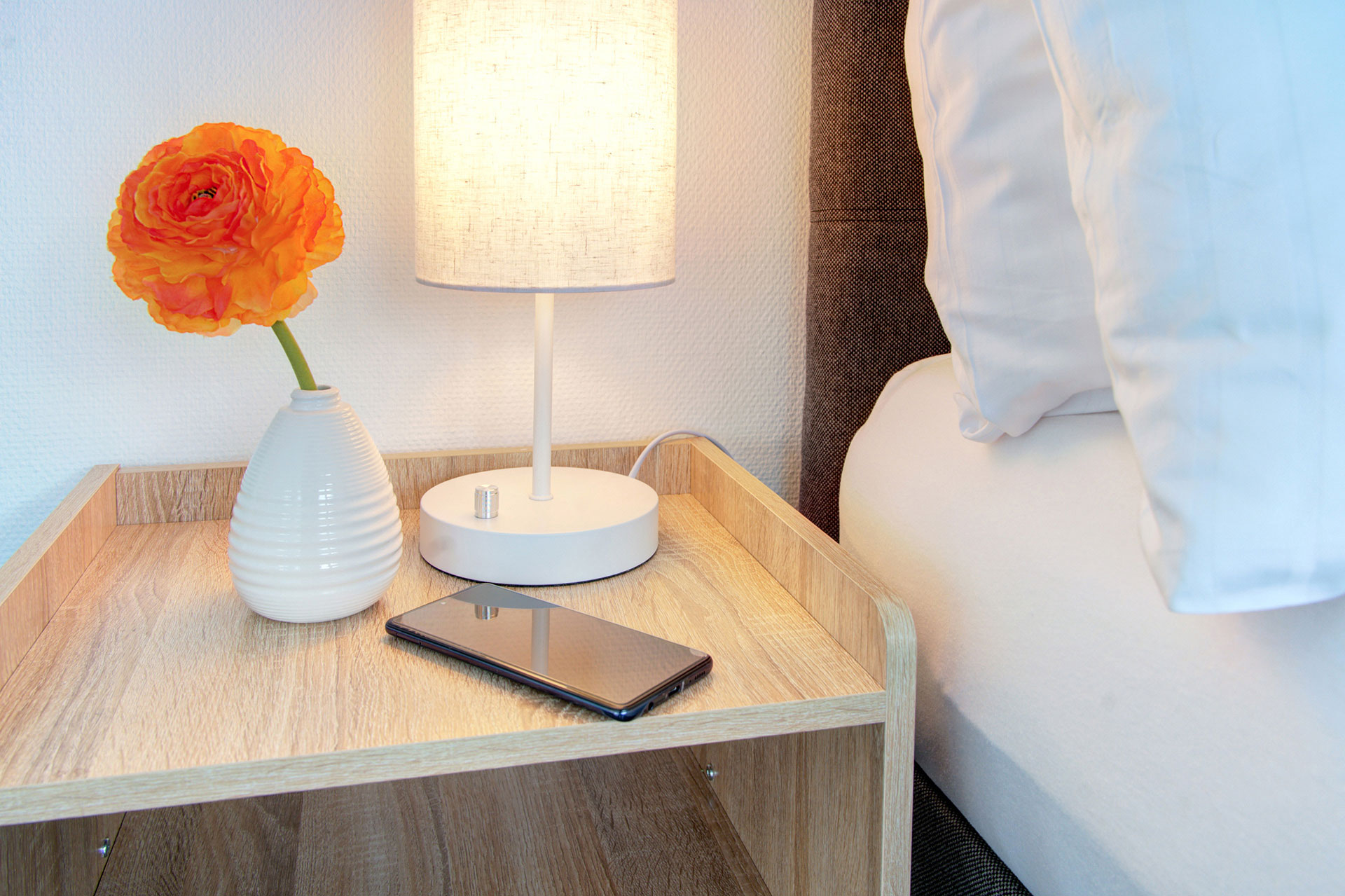 bett und nachttisch mit handy und orangener mohnblume