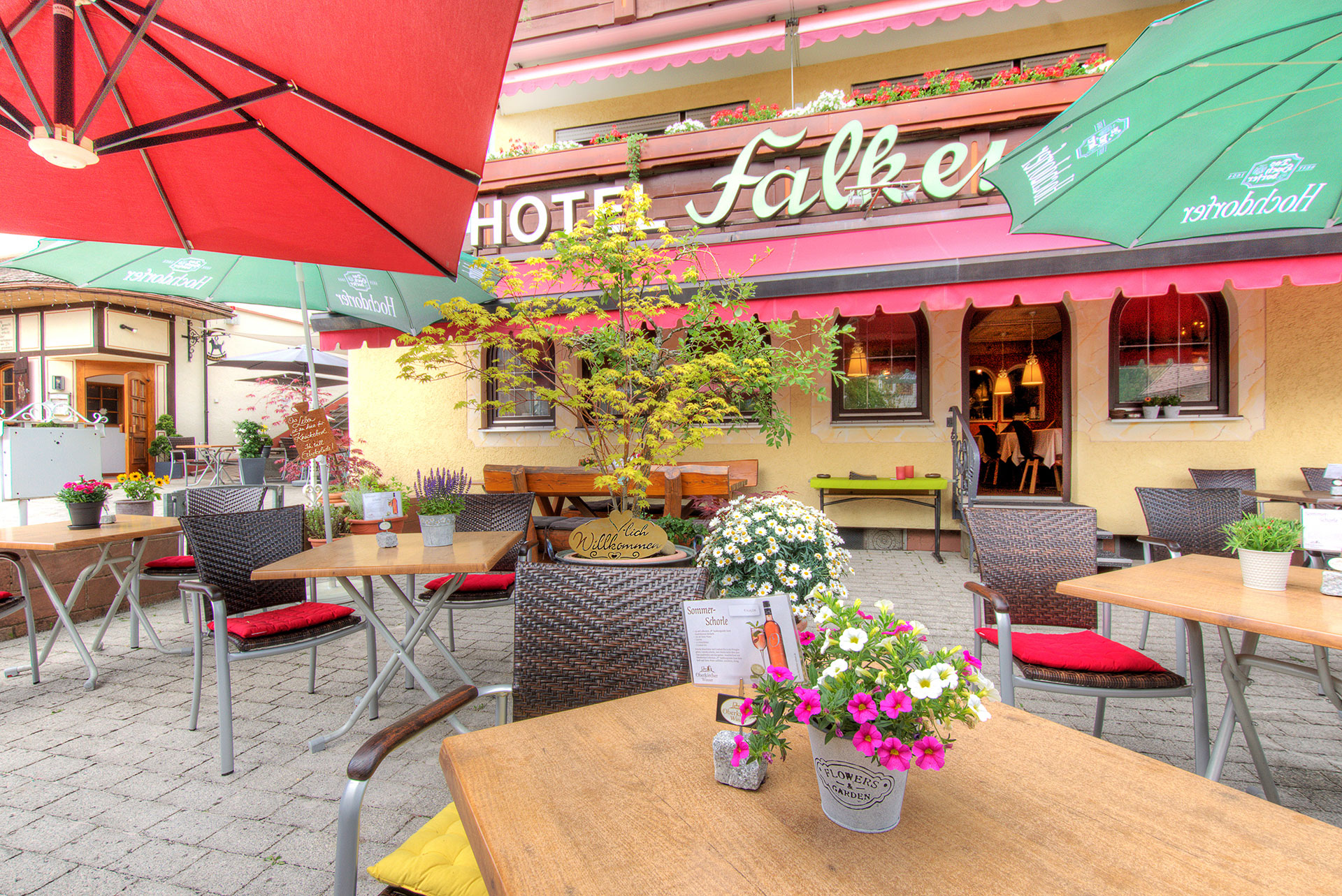 hotelfoto biergarten mit blick auf tisch mit blumen sowie im hintergrund das hotelschild