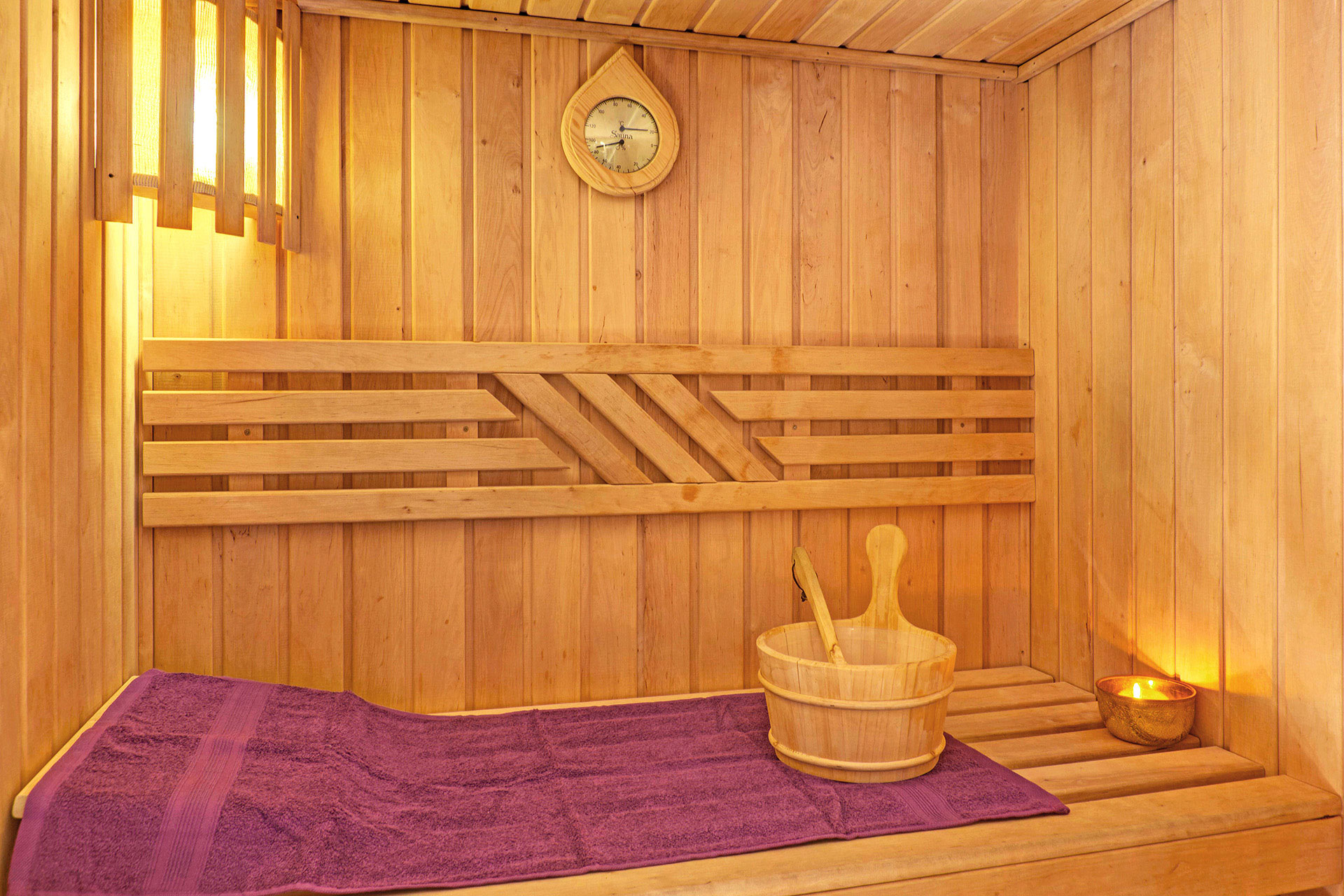 sauna mit saunakübel teelicht und lila handtuch in hotel