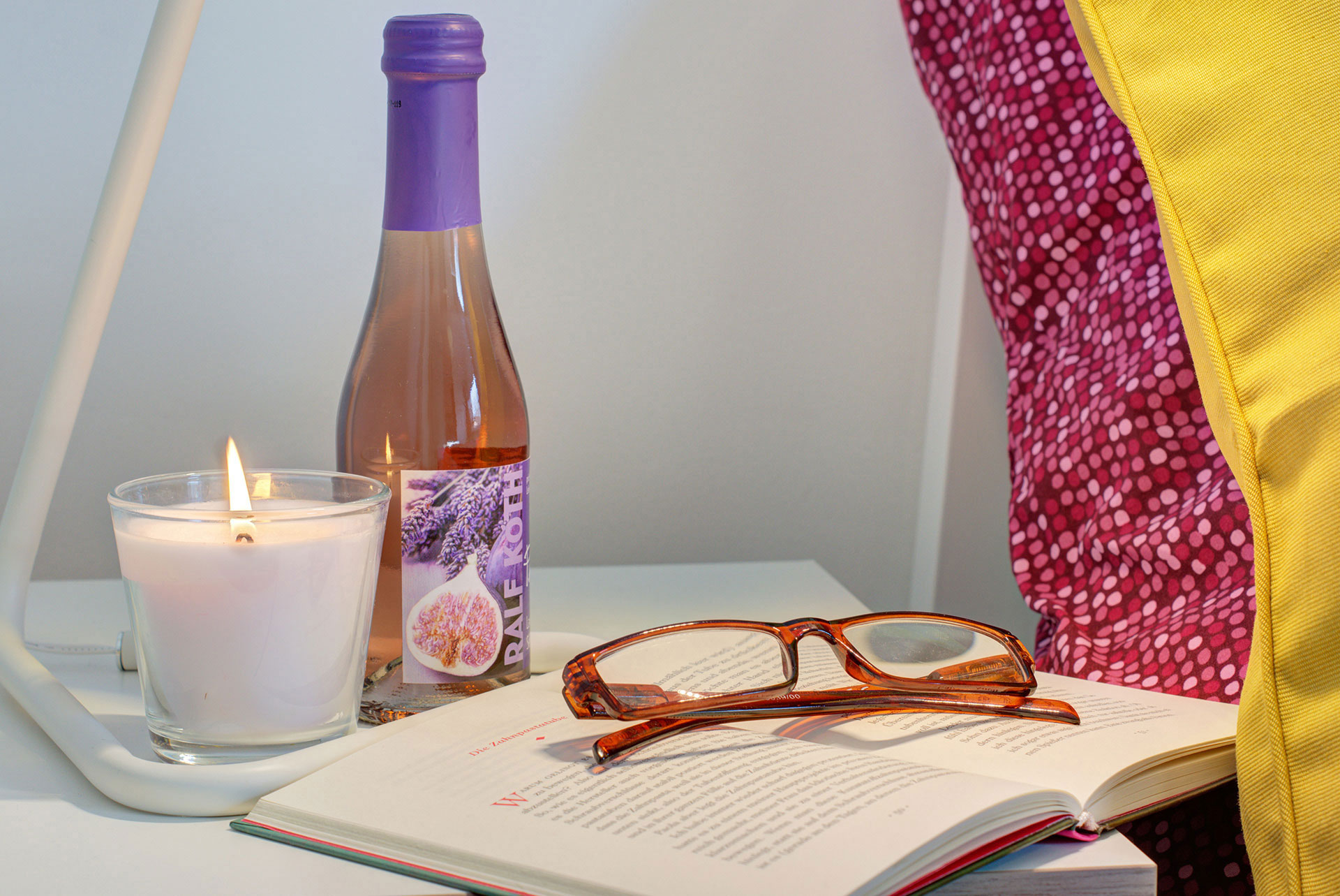 nachttisch mit sektfläschchen teelicht buch und brille in apartment