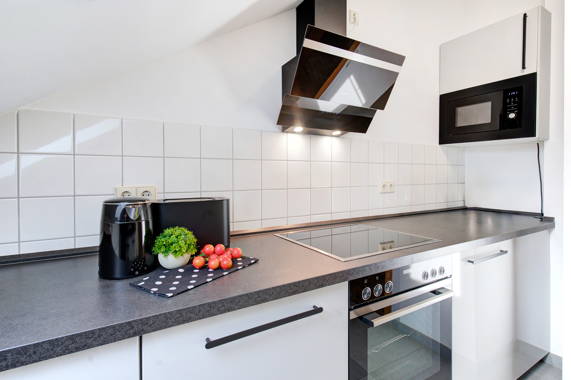 schwarzweise moderne Küche der ferienwohnung mit schräger Kopffreihaube über dem Ceranfeld