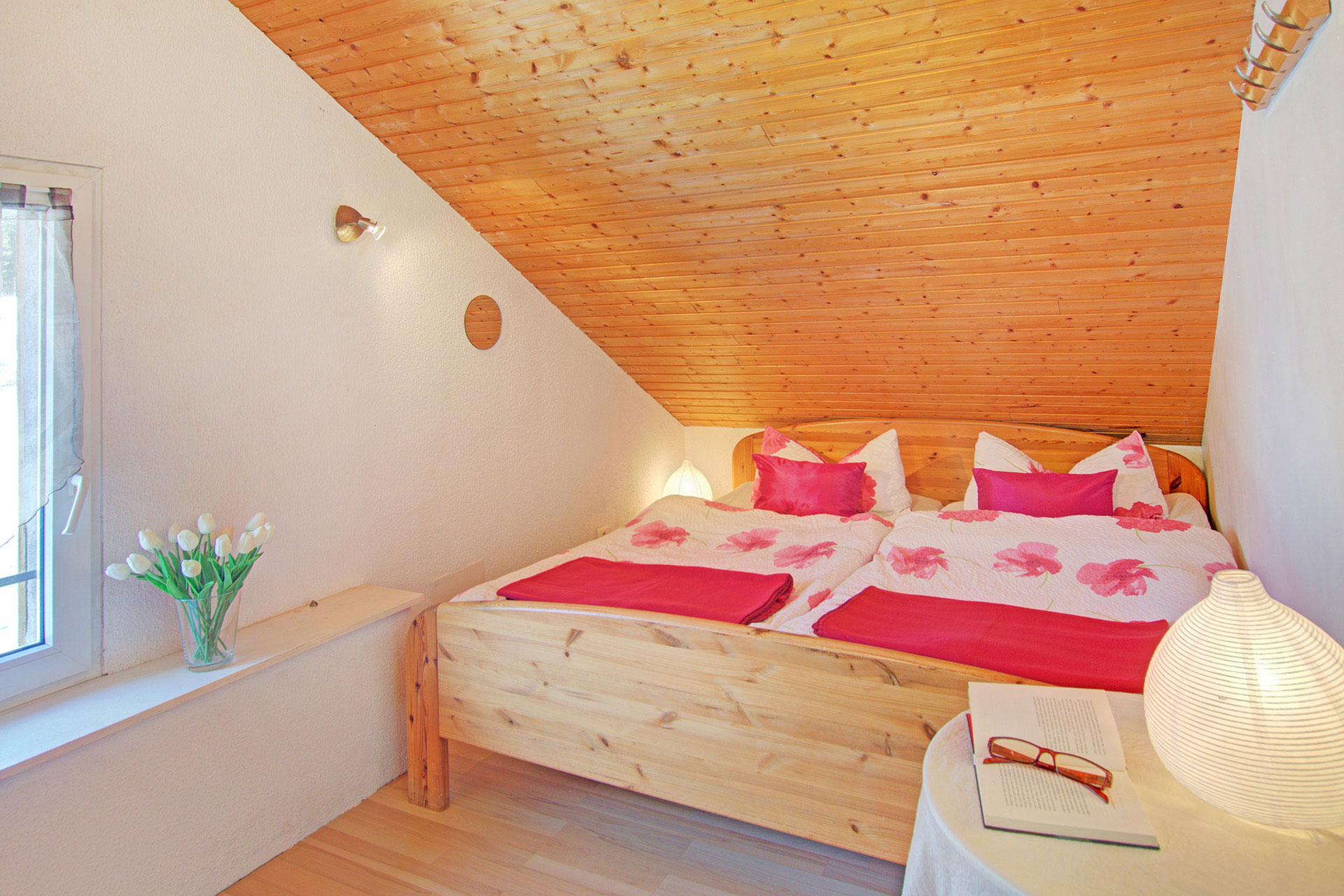 ferienhaus foto doppelzimmer mit rosaner bluetenbettwaesche und viloetten kissen mit weisen tulpen und seitlich mit lampe