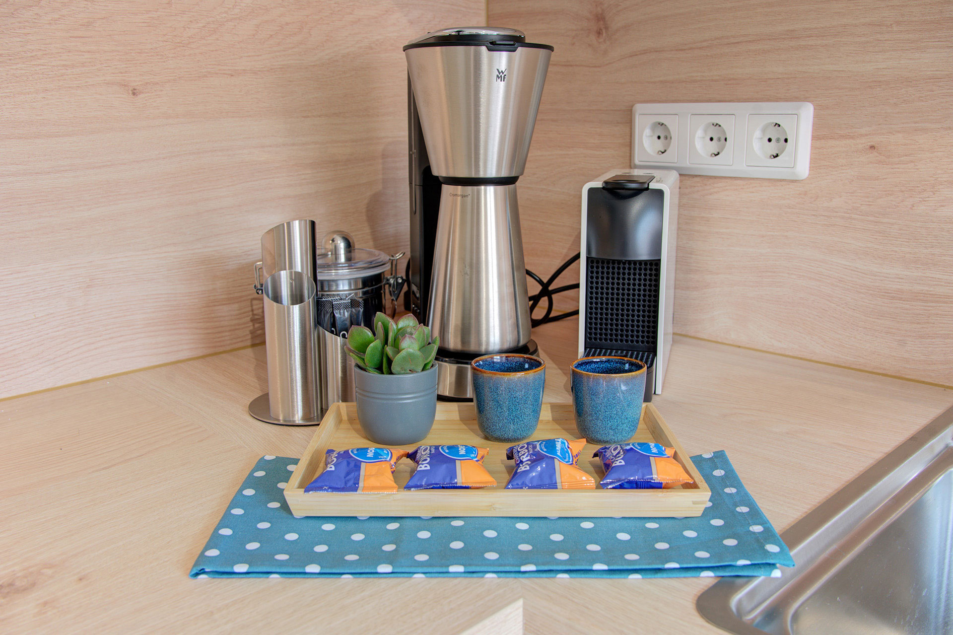 kombination aus espressomaschine kleine pflänzchen geschirrtuch kekse in ferienwohnung