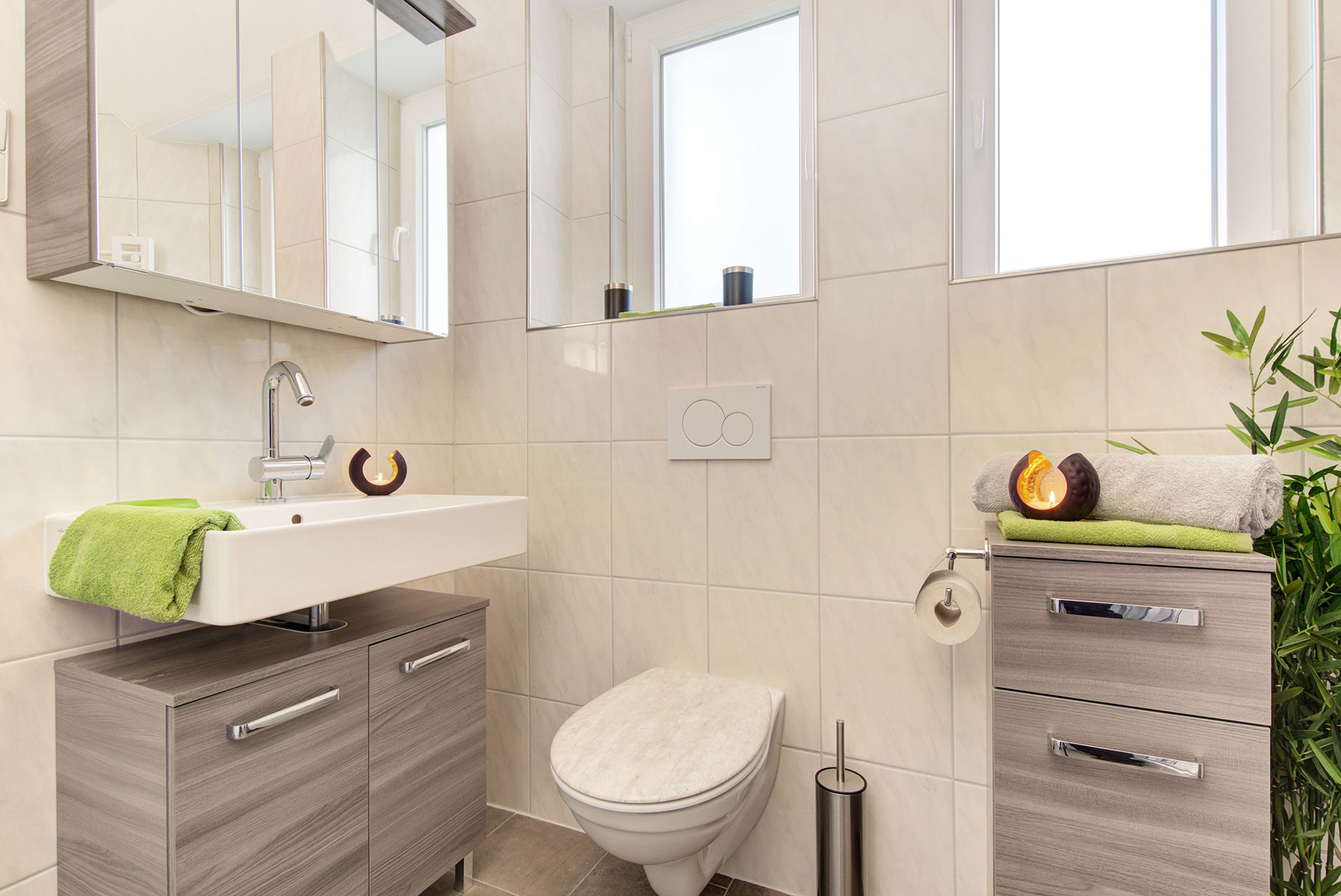 kleines Bad mit waschbecken und wc sowie schwarzgoldene teelichter und grüne handtücher in ferienwohnung