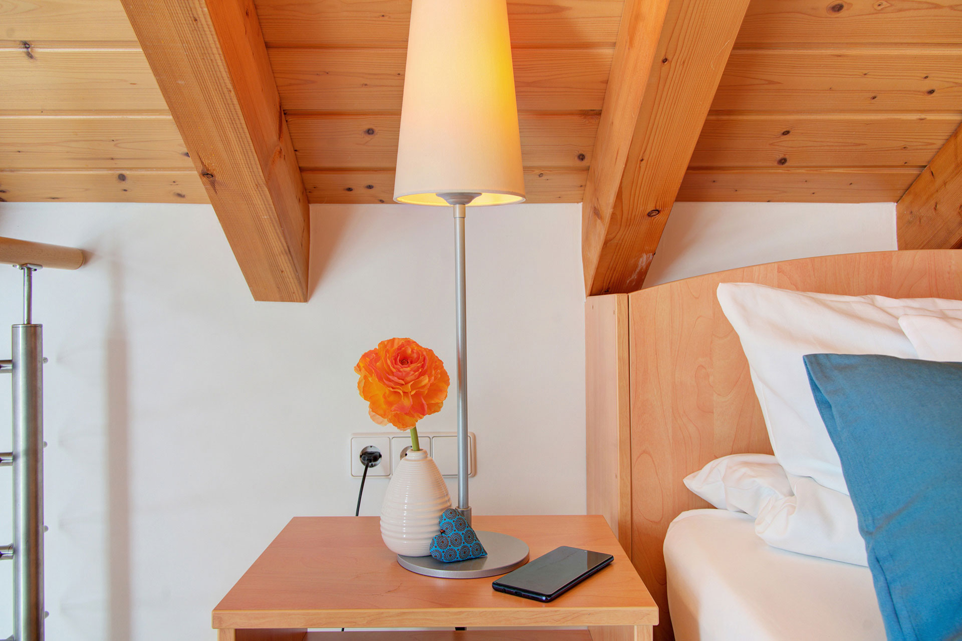 nachttisch unter dachschräge mit brennender lampe und kleiner blumenvase