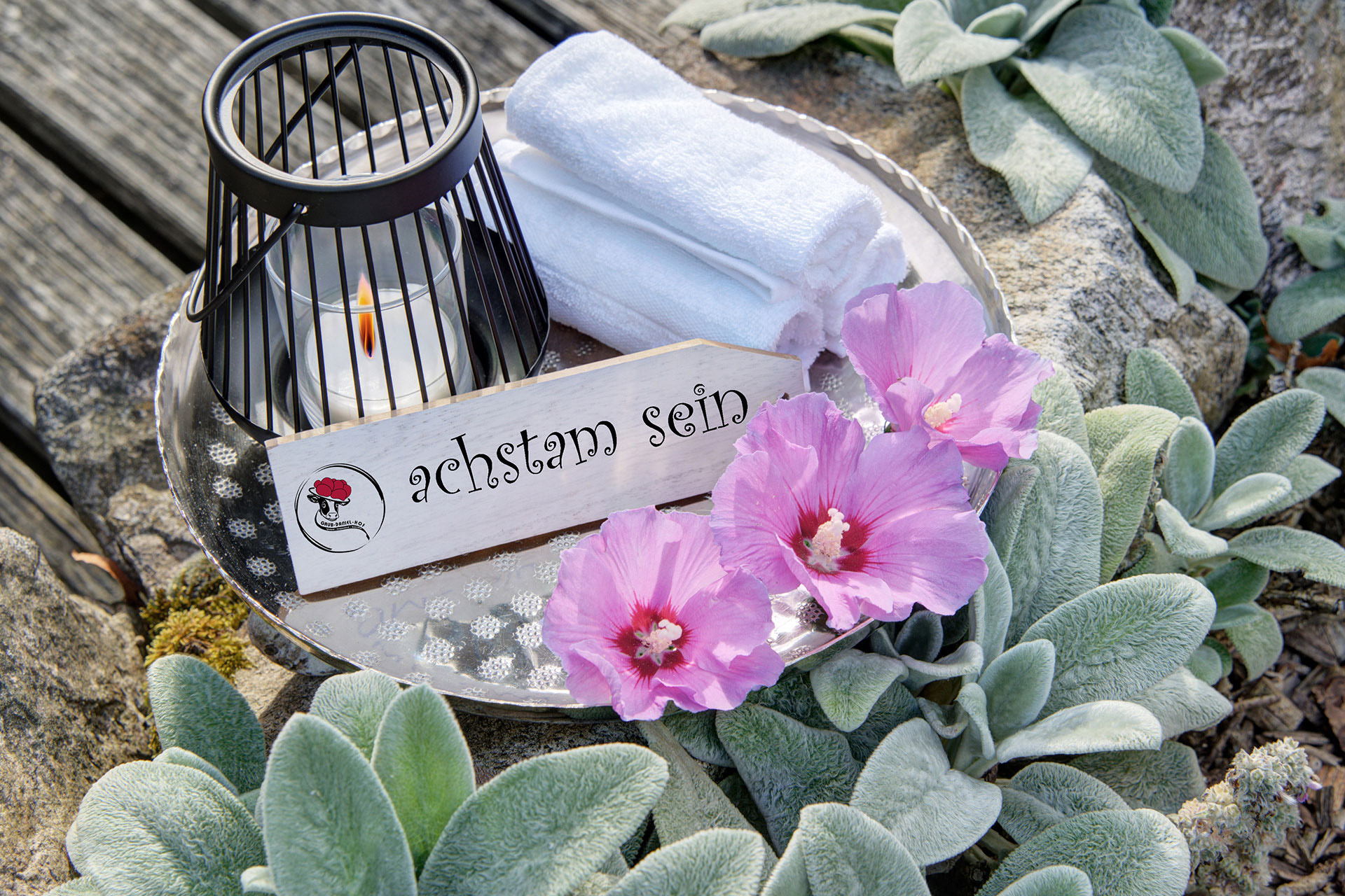 metalltablett mit Teelicht handtuch und hibiskusblüten sowie schild achtsam sein im Garten von Ferienhof