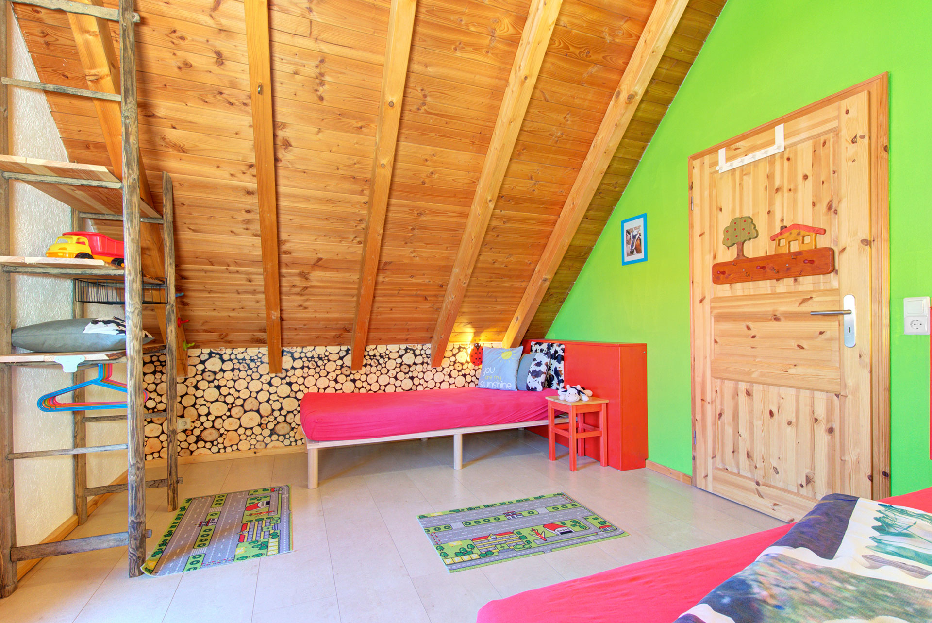 rotes kinderbett in grossem Dachschrägeraum mit Spielteppich im ferienhaus