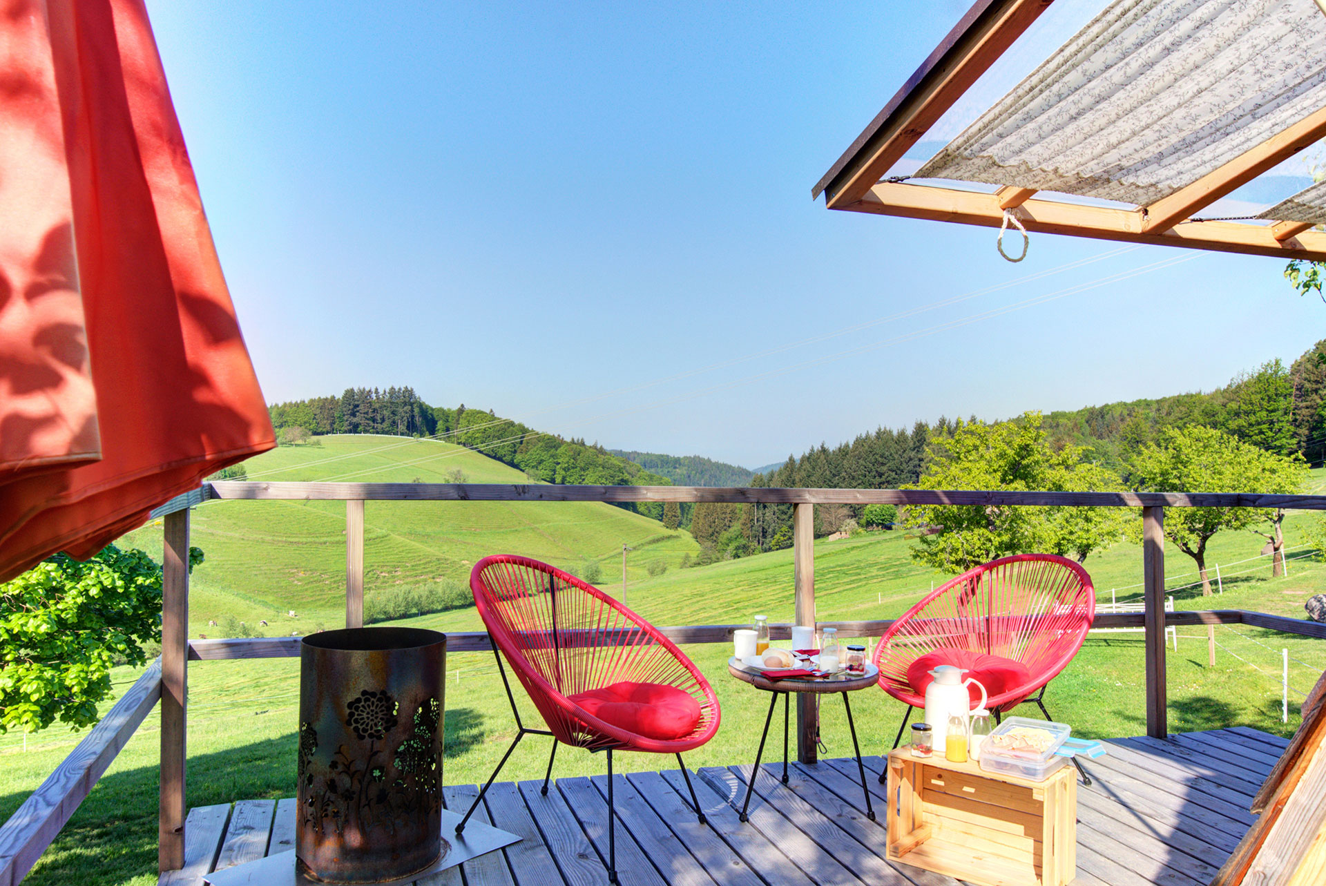 private Terrasse mit zwei roten gemütlichenStühlen und tisch vorm Holzzelthaus