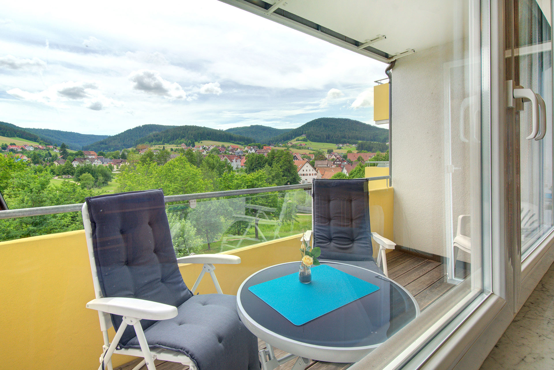 foto ferienwohnung blick von innen auf balkon mit zwei stuehlen und tisch im hintergrund die landschaft