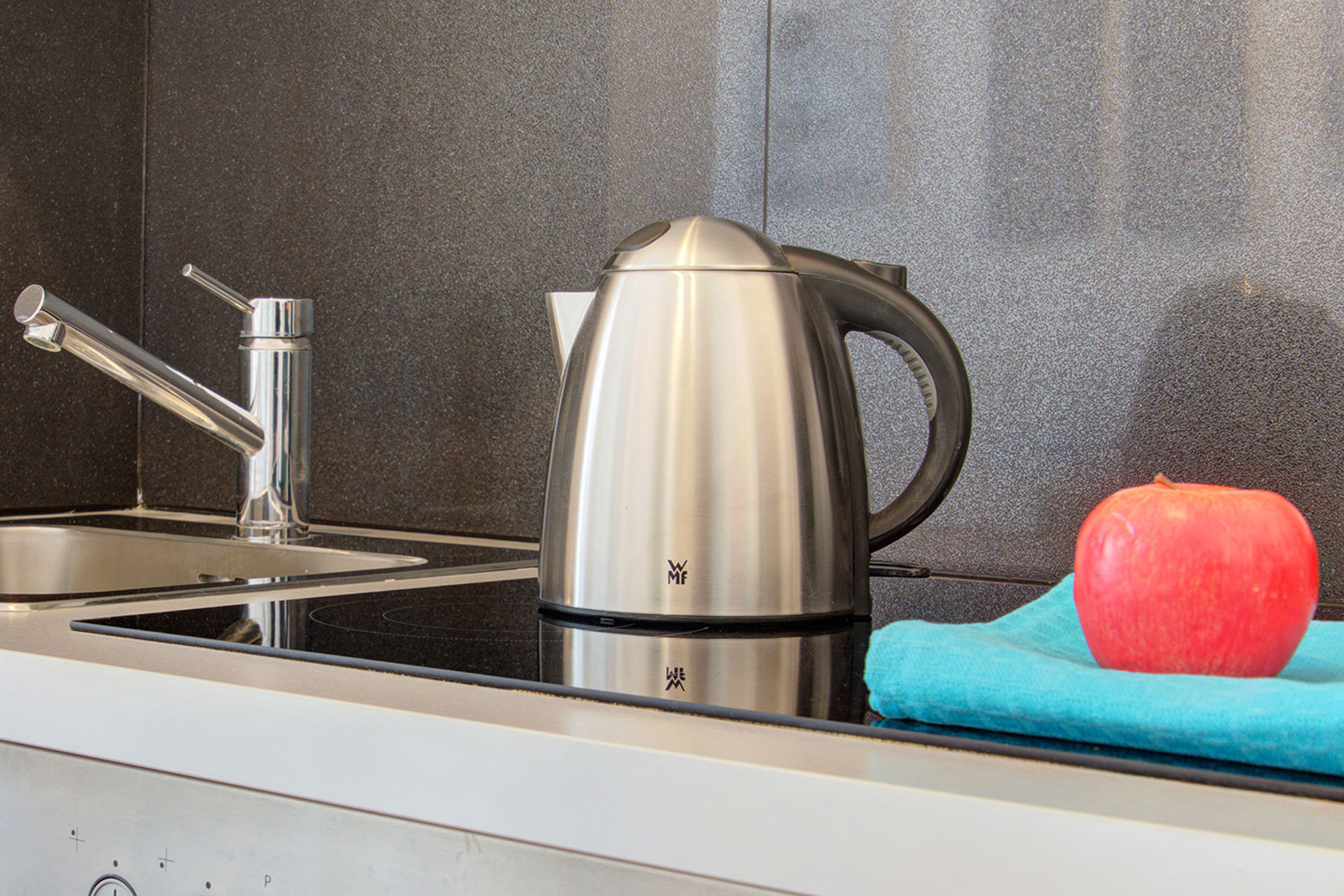 fotografin dekoriert herd mit türkisem geschirrhandtuch und apfel und wasserkocher