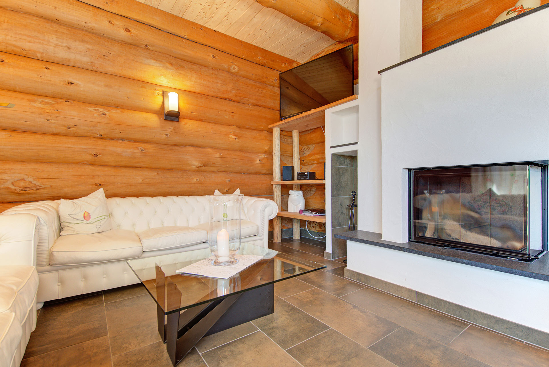 Gemütliches Ferienhaus-Wohnzimmer aus Holz, Ledersofa in Creme, Kamin ohne Flamme