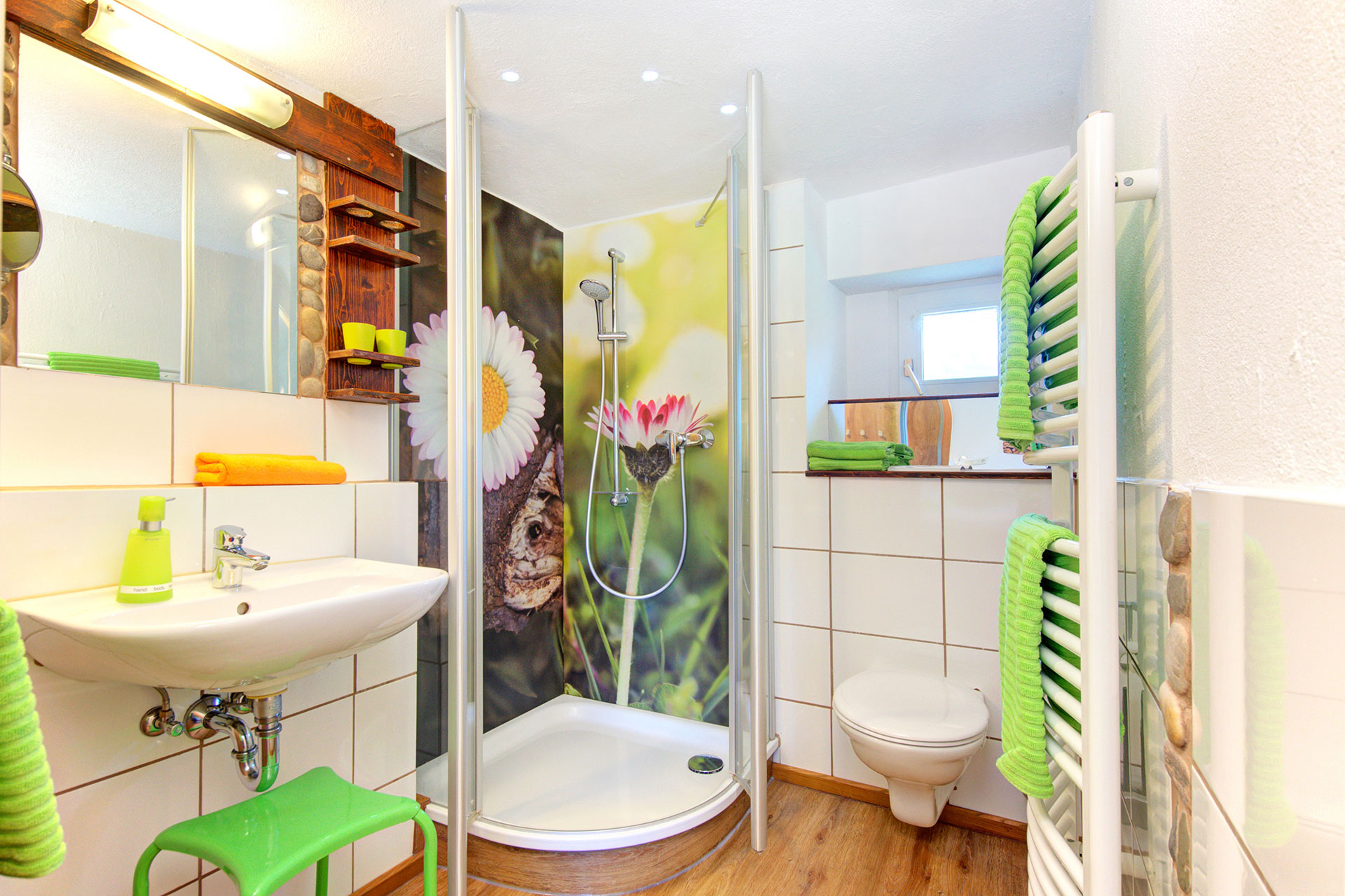 badezimmer einer ferienwohnung mit dusche und gänseblümchenposter sowie grüne handtücher