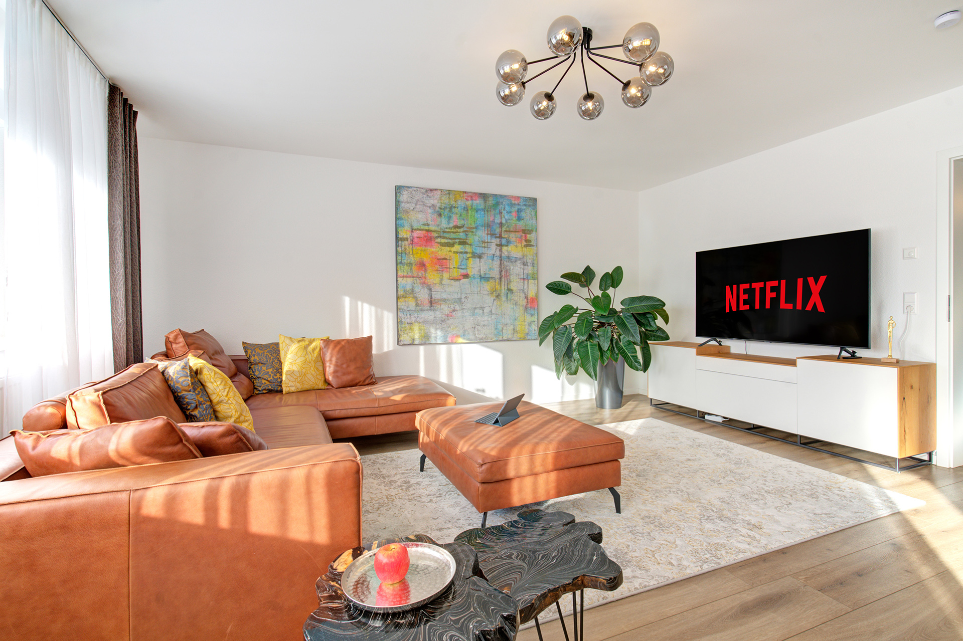Wohnzimmer der Ferienwohnung mit grosser brauner Ledergarnitur, buntem Bild und hochauflösendem TV-Monitor - vom airbnb fotograf