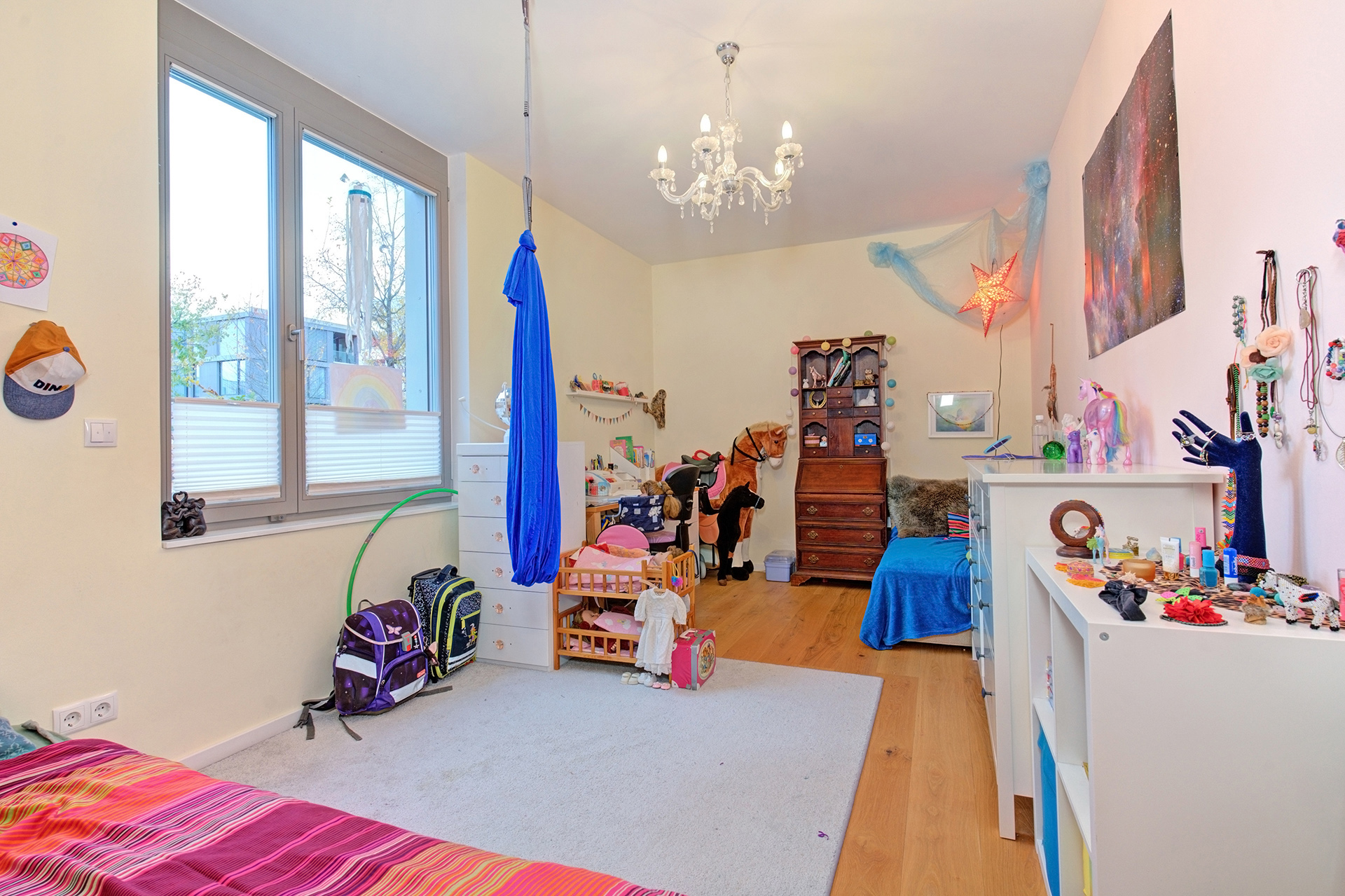 Kleines helles Kinderzimmer mit Bett Kommode Leuchter und bunten Spielsachen 