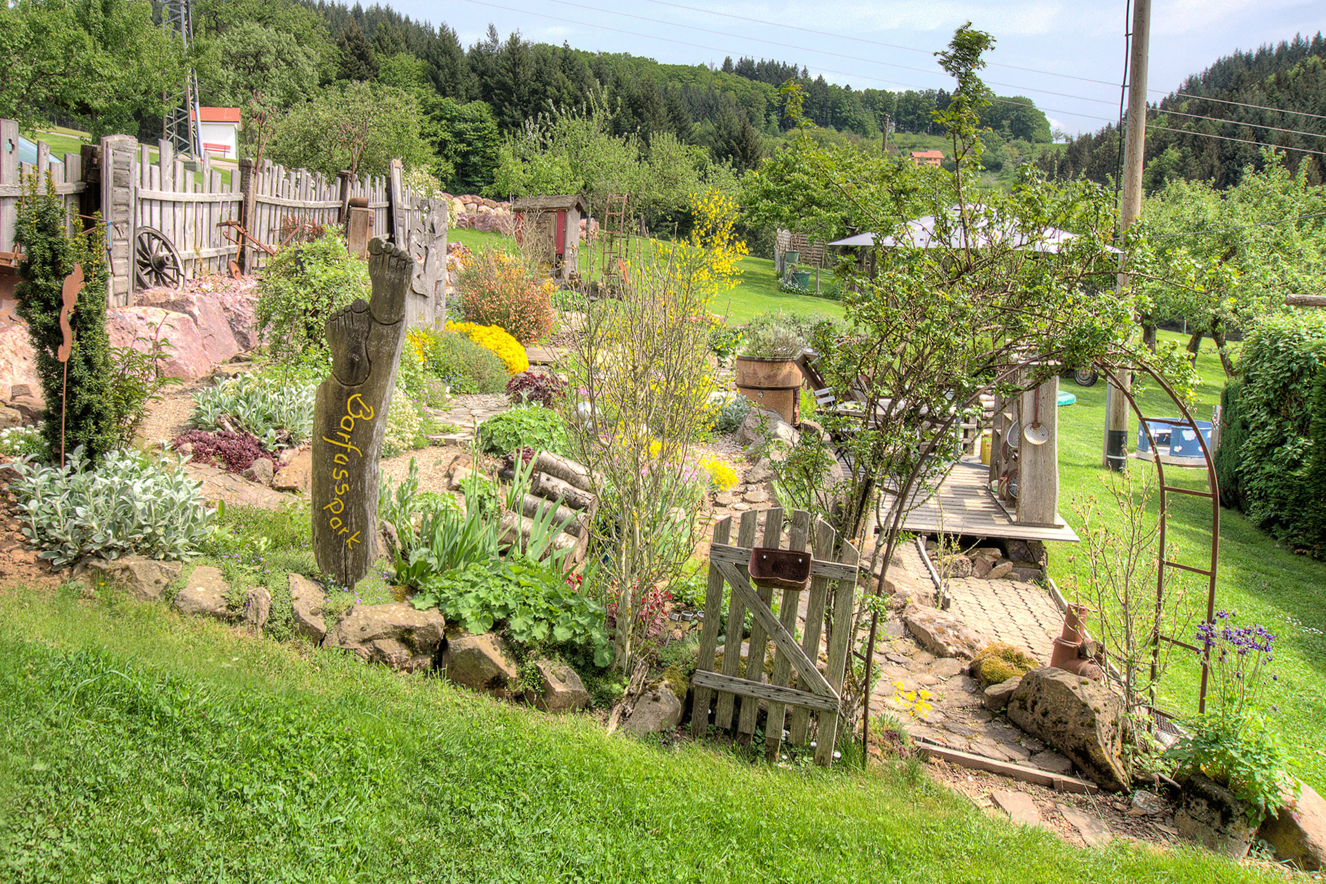 barfusspark mit rosenzauneingang und vielen kräutern beim ferienhof