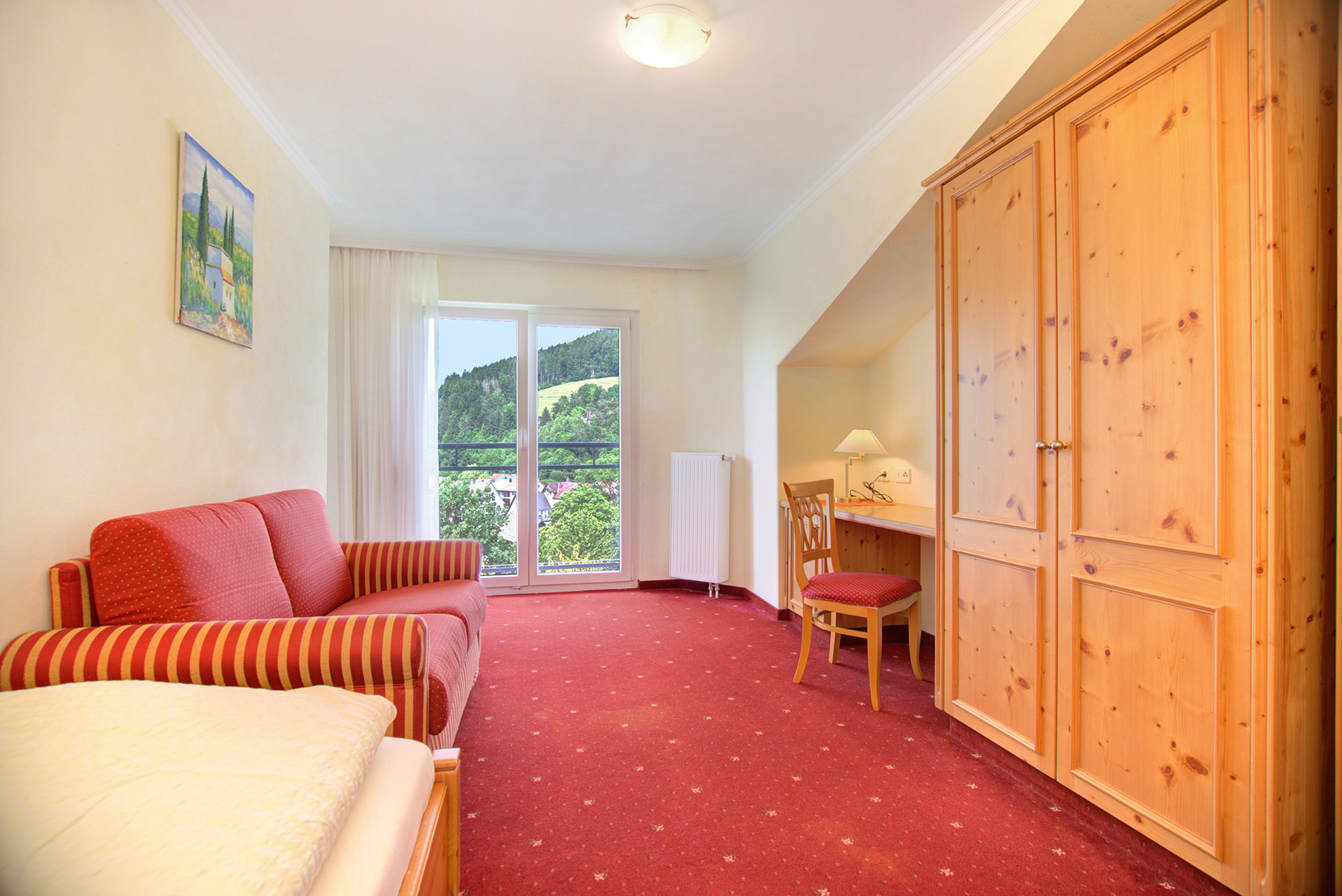 foto ferienwohnung einzelzimmer mit rotem sofa und arbeitsbereich sowie fensterblick in den garten