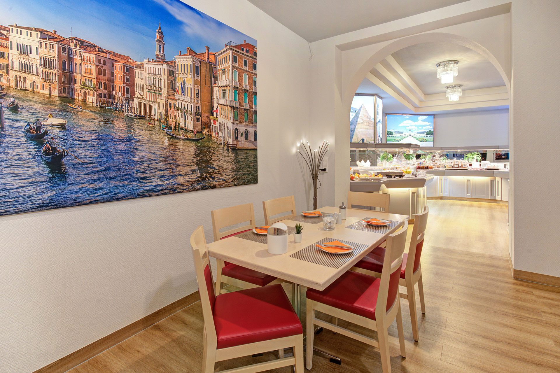 gedeckter tisch vor foto venedig mit blick auf beleuchtetes frühstücksbüffet in hotel