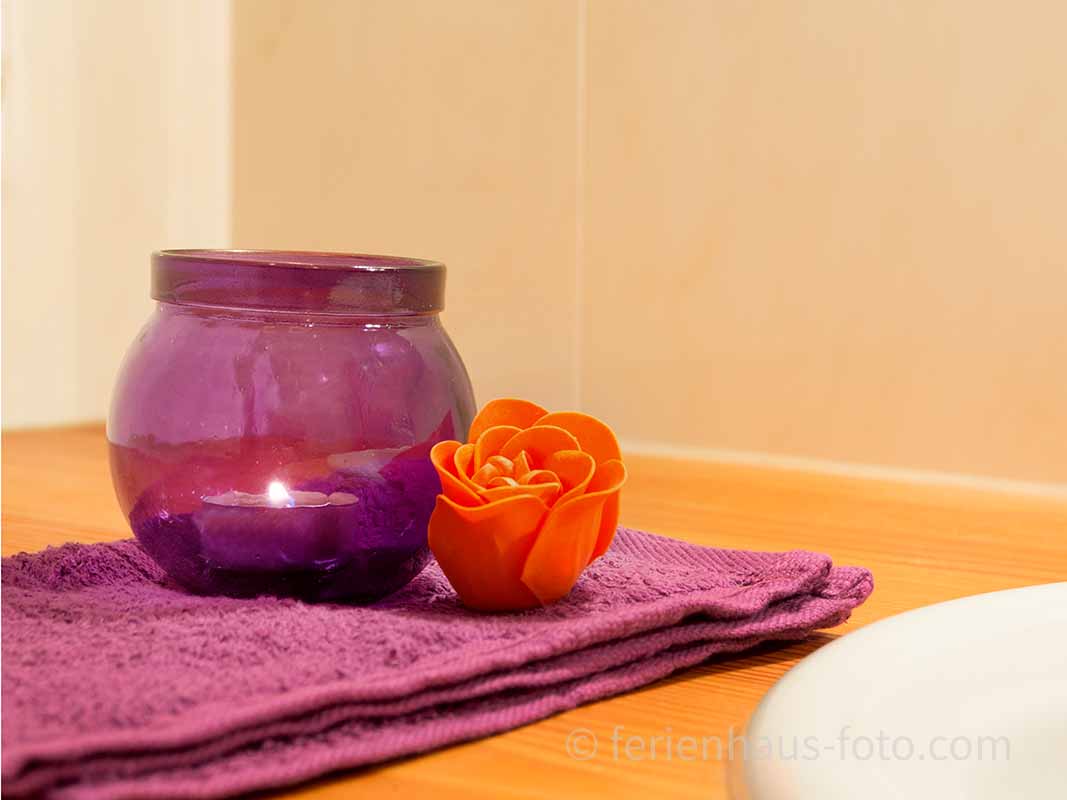 fotografin dekoriert lila handtuch und lila teelicht mit kleiner oragener rose
