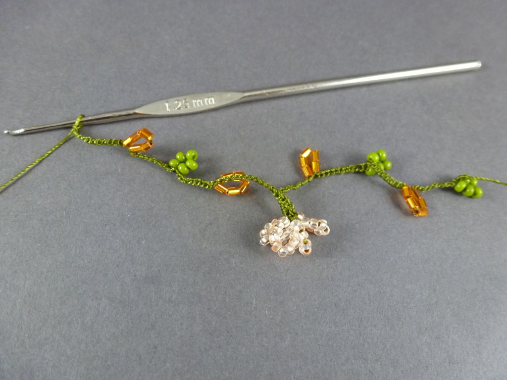 15. Häkeln Sie 10 LM, 5 orange Perlen, 10 LM, 5 grüne Perlen, 10 LM, 5 orange Perlen, 15 LM, danach die nächste Blüte. 