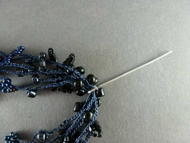 31. Hängen Sie alle gehäkelten Stränge in den Haken, so daß die Perlen der Farbe 1 jeweils rechts und links des Stiftes zu liegen kommen.