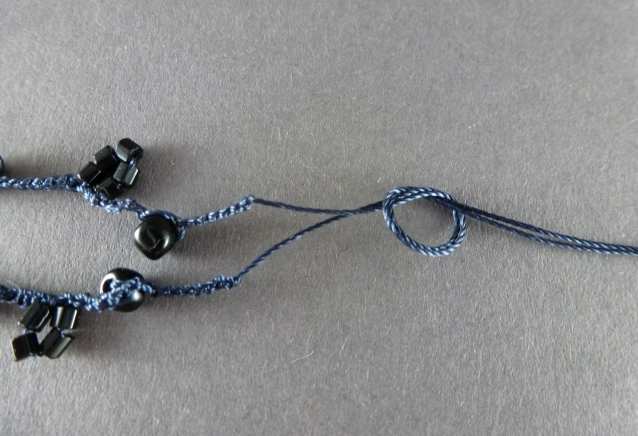 21. Wenn Sie alle Perlen verhäkelt haben, schneiden Sie das Garn ca. 10cm lang ab und ketten ab, so daß die Maschen sich nicht mehr auflösen können. Nehmen Sie Anfang und Ende des Garns zusammen und verknoten Sie es. Noch nicht festziehen!