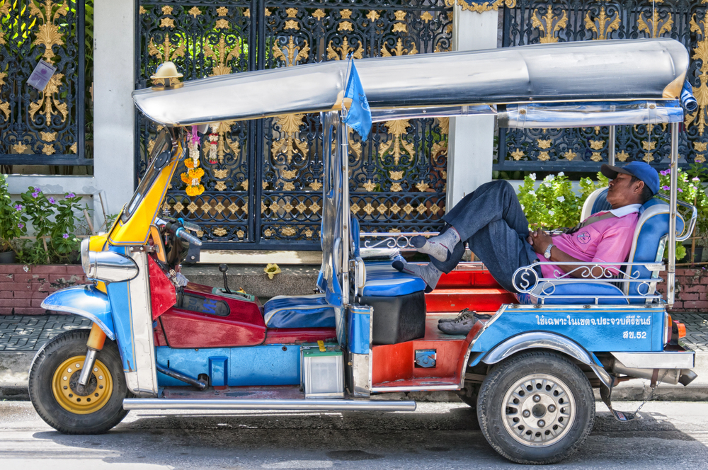 Ein thailändischer Tuk-Tuk-Fahrer hält in der Mittagshitze ein Nickerchen auf der Rückbank seines bunten Fahrzeugs.