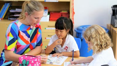Lehrperson der Deutschsprachigen Schule in Bangkok erklärt zwei Mädchen eine Aufgabe. (Bild: RIS Swiss Sektion - Schule Bangkok)