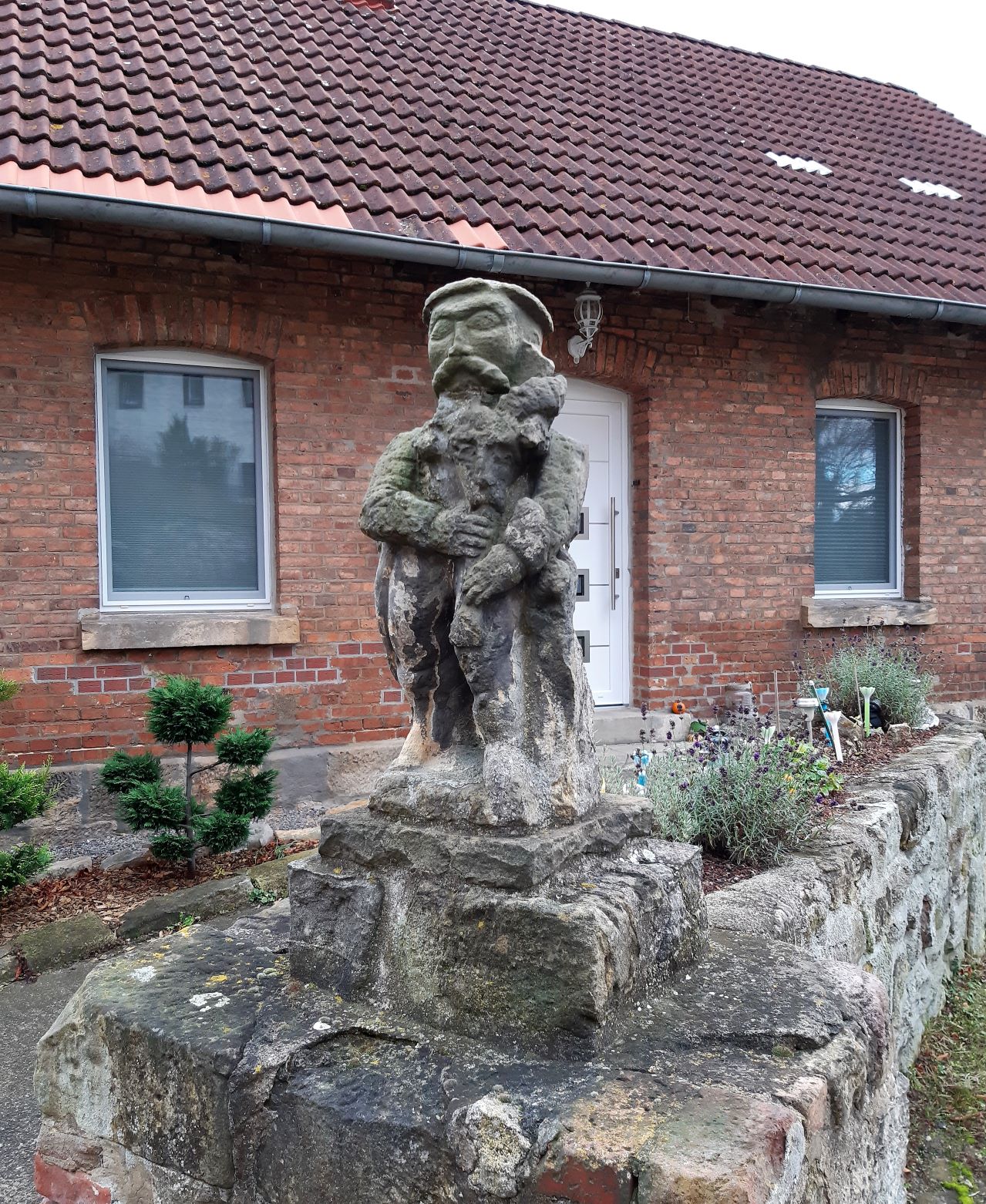 Die Steinfigur erinnert an einen südländischen Schafhirten oder Nomaden, scheinbar mit einem Dudelsack