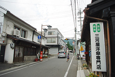 軒下にぶら下がる黄色い子供傘が目印の「三河屋洋傘店」さん。はす向かいの古民家がナノグラフィカの喫茶室「金斗雲」です