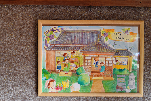 「さくら工房」三條さん作の絵画にはいろいろな人たちが集う、カナルファームの母屋が描かれています