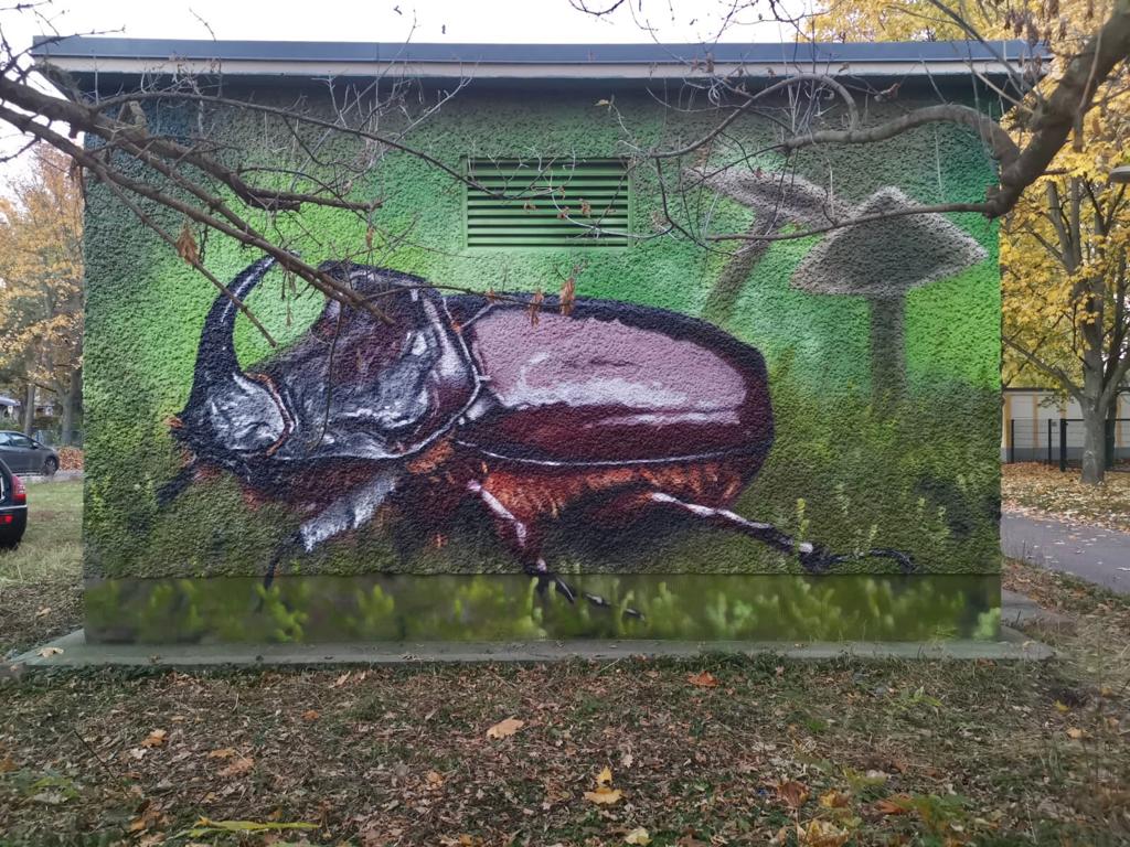 uffälliges Streetart-Kunstwerk auf einem elektrischen Verteilerhäuschen mit Hirschkäfer, Pilz und Schnecke. Hochwertige Wandmalerei als Vandalismusschutz und zur ästhetischen Aufwertung des öffentlichen Raums durch Appolloart, deutschlandweit umsetzbar.