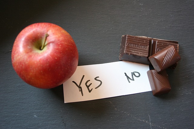 Apfel und Schokolade vor Zettel Yes und no zum Thema Süßigkeiten und Heißhunger und Gewohnheiten