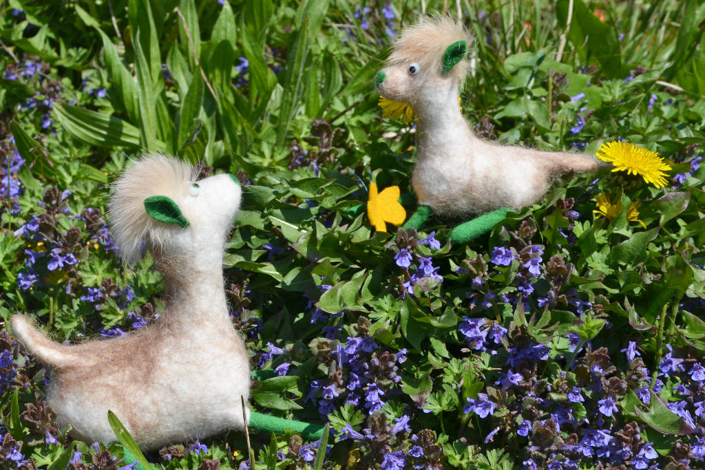 Zwischen blauen Blümchen sitzen weiße gefilzte Alpakas mit grünen Füße und Ohren