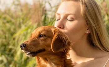 Frau im Gegenlicht, die ihrem Hund ein Bussi gibt – emotionales People- und Portraitfoto im Freien