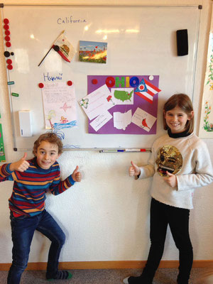 Children proudly presenting their completed English learning projects at Custom Kids.
