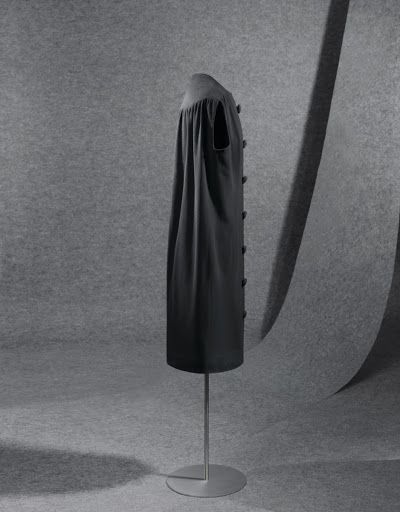 El vestido, de estructura trapezoidal, es largo por debajo de la rodilla. Con cuello a la caja, sin mangas y abierto por delante de arriba abajo. Lleva canesú, pinza de cadera a pecho, y de cadera a centro de la sisa. Los botones, grandes, van forr, 1957