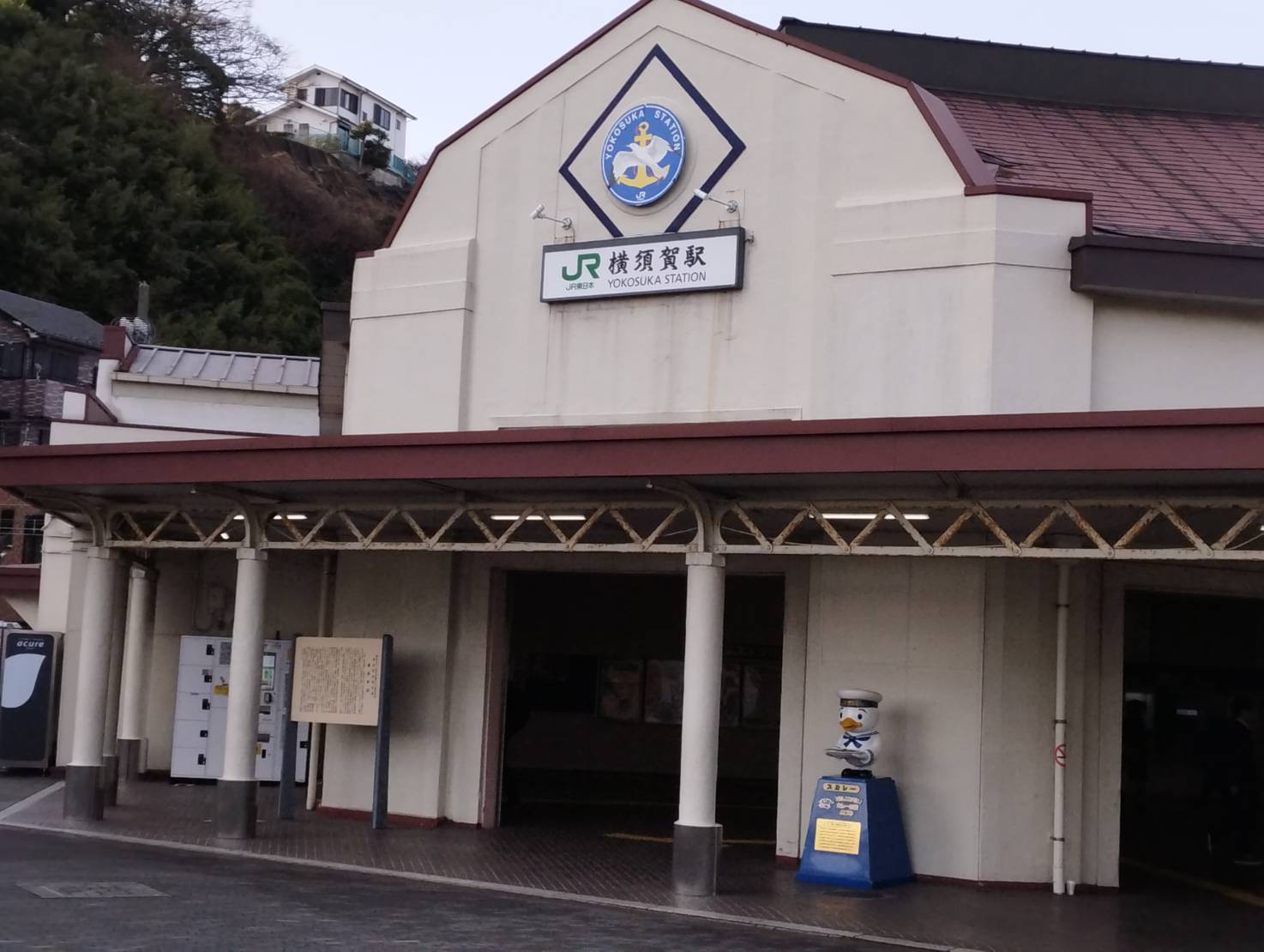 JR横須賀駅の駅舎とマスコット像 赤い屋根が印象的なJR横須賀駅。海軍ゆかりのマスコット像が出迎えてくれます。