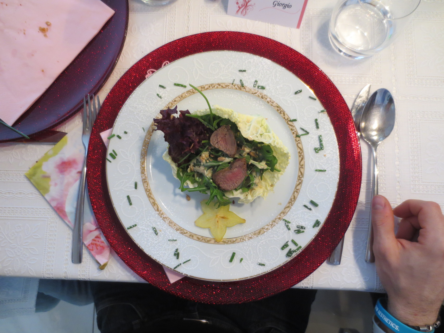 Rucola, Parmigiano e Filetto d'Agnello (Knackfrischer Rucola-Salat im Wirz-Körbchen, verziert mit etwas Lollo Rosso, Parmesanhobel und warmen Lammfilet-Streifen)