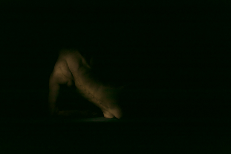 Fotografia a colori di nudo artistico di particolare di corpo femminile immerso nell'oscurità