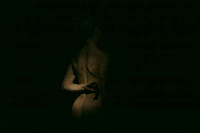 Fotografia a colori di nudo artistico di particolare di corpo femminile immerso nell'oscurità