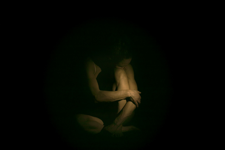 Dettaglio di corpo femminile che emerge dall'oscurità, fotografia intima in stile chiaroscuro di Alessandro Tintori.
