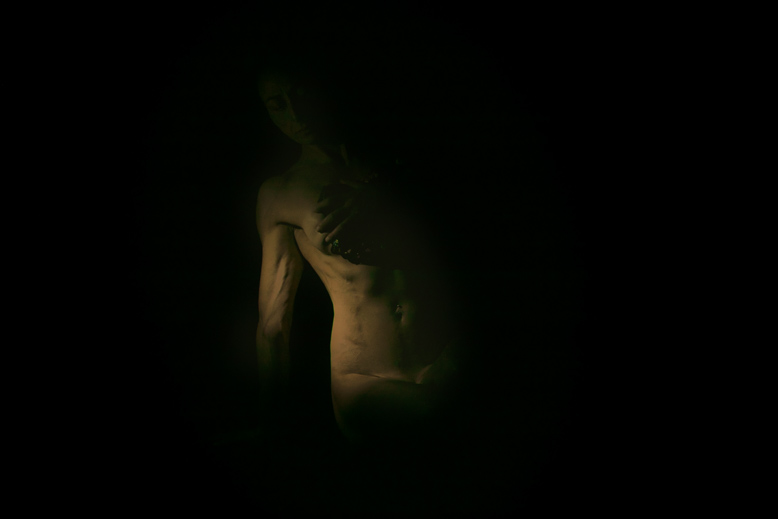 Dettaglio di corpo femminile che emerge dall'oscurità, fotografia intima in stile chiaroscuro di Alessandro Tintori.