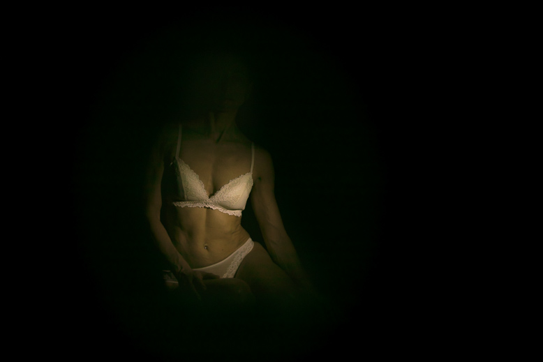 Dettaglio di corpo femminile che emerge dall'oscurità, fotografia intima in stile chiaroscuro di Alessandro Tintori.