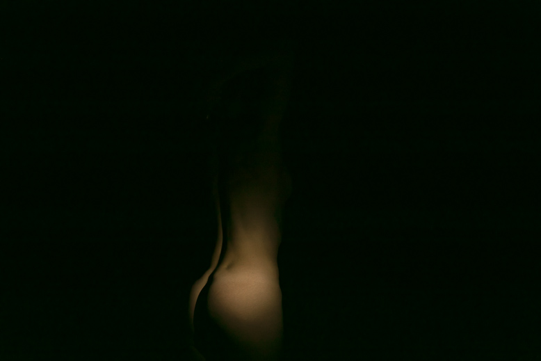 Fotografia a colori di nudo artistico di particolare di corpo femminile immerso nell'oscurità