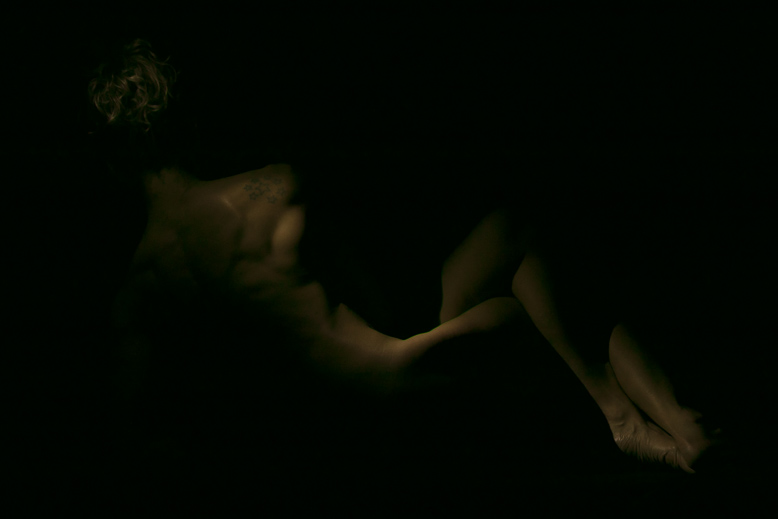 Fotografia a colori di nudo artistico di particolare di corpo femminile immerso nell'oscurità