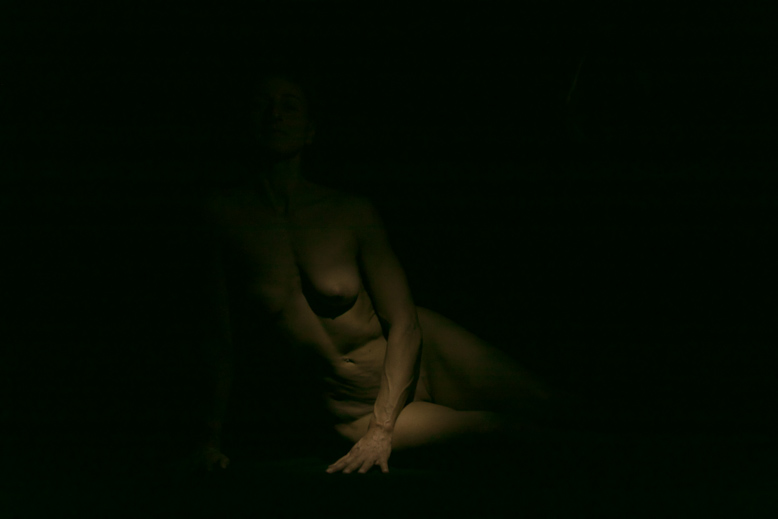 Fotografia a colori di nudo artistico di particolare di corpo femminile immerso nell'oscurità